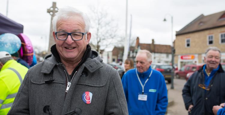 Older man standing outside with a coat on smiling directly at the camera