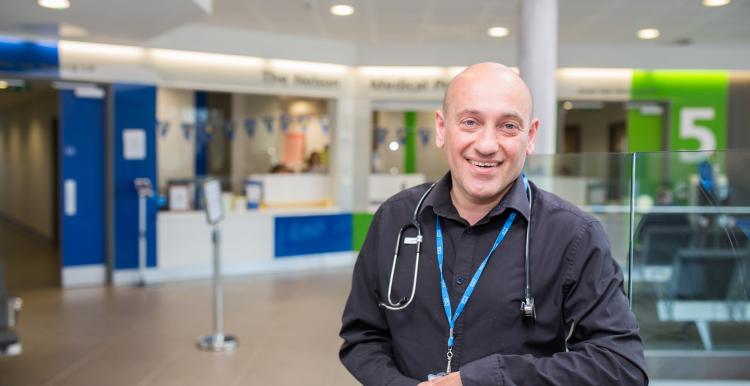 Man in medical setting wearing NHS lanyard smiling at the camera 